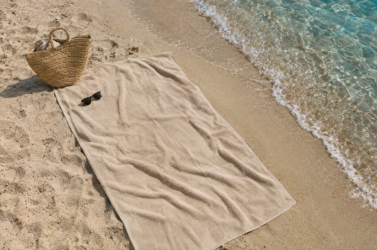 Serviette de plage beige étendue sur le sable au bord de l'eau, avec un panier en paille Image